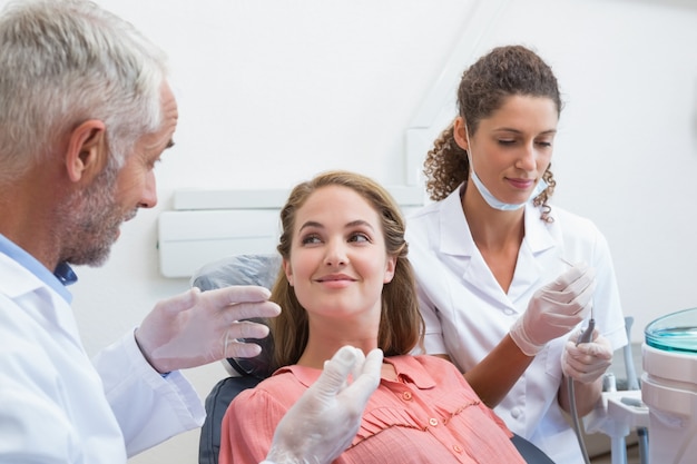 Dentista parlando con paziente mentre infermiera prepara gli strumenti