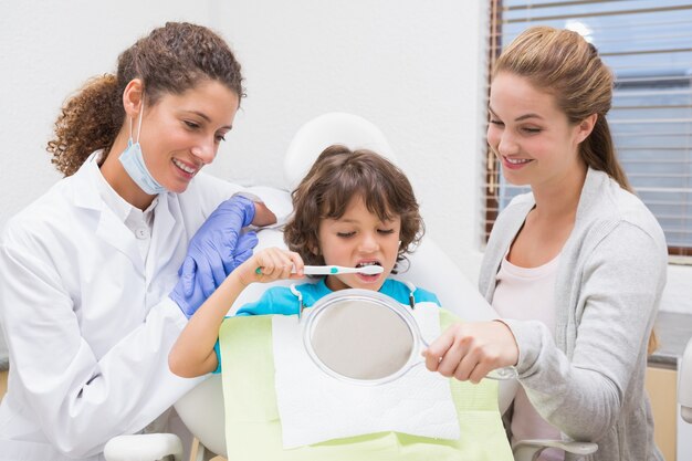 Dentista pediatrico che mostra a ragazzino come lavarsi i denti con sua madre