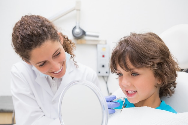 Dentista pediatrico che mostra a ragazzino i suoi denti nello specchio