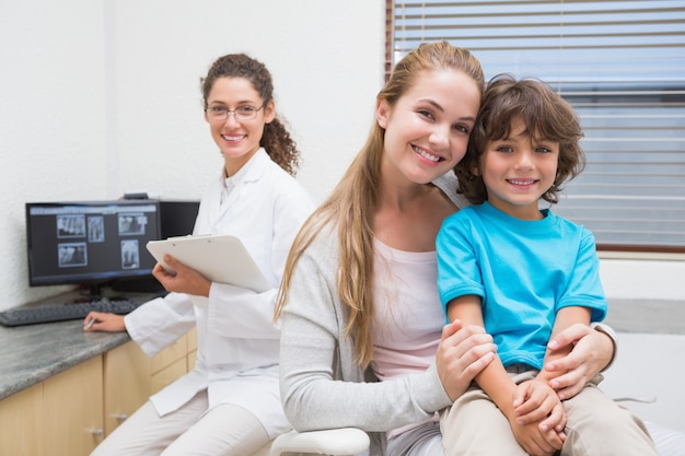 Dentista pediatrico che sorride alla macchina fotografica con il ragazzino e sua madre