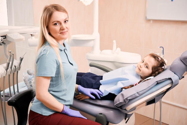 Dentista pediatrico seduto accanto a una bambina adorabile in studio dentistico