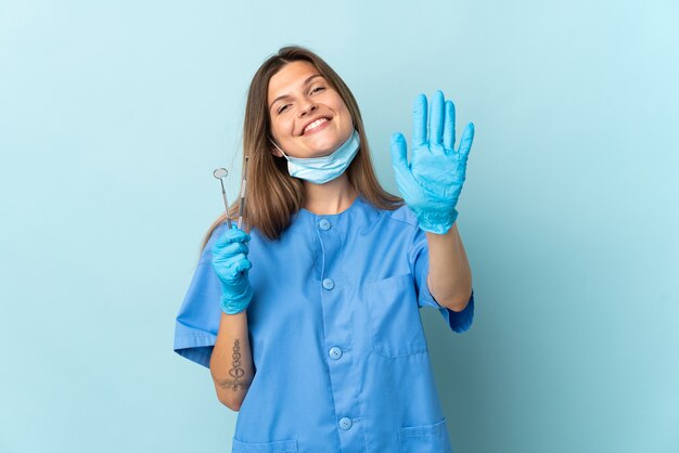 Dentista slovacco che tiene gli strumenti isolati sulla parete blu che conta cinque con le dita