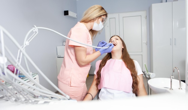 Dentisti che usano un trapano dentale durante l'esame della bocca di una ragazza in clinica Trattamento professionale in clinica dentale