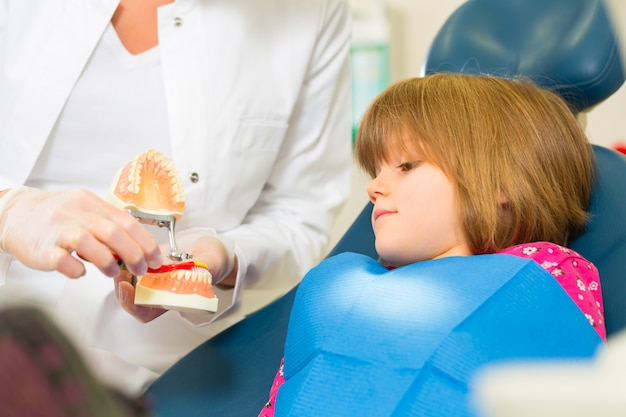 Dentisturgery detiene la protesi e spiega un bambino paziente con uno spazzolino da denti