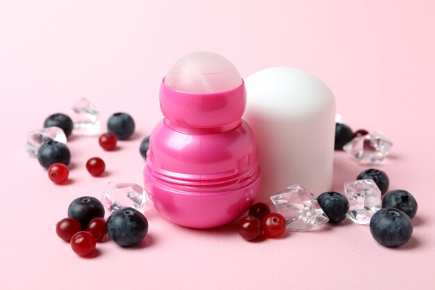 Deodorante roll-on, cubetti di ghiaccio e frutti di bosco su sfondo rosa