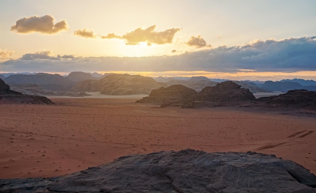 Deserto di Wadi Rum in Giordania, montagne rocciose con campo di sabbia piatto intorno, sfondo nuvole tramonto pomeridiano