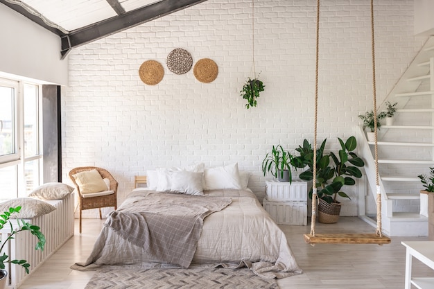 Design della camera da letto di lusso in un cottage rustico in stile minimalista. pareti bianche, finestre panoramiche, elementi decorativi in legno sul soffitto, altalene di corda nel mezzo di una stanza spaziosa.
