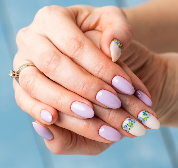 Design delle unghie. Mani con lilla brillante e bianco manicure con fiori primaverili. Primo Piano Di Mani Femminili. Nail art.