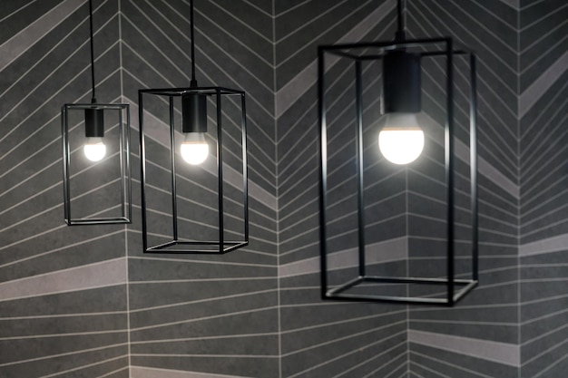 Design interno creativo della stanza decorata con luci illuminanti moderne appese in cornici metalliche rettangolari di colore nero contro le piastrelle grigie simmetriche della parete