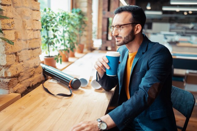 Designer che beve caffè. Bello designer d'interni barbuto che beve caffè con una pausa al lavoro