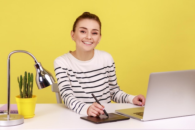 Designer creativo donna seduto sul posto di lavoro con tavoletta grafica e computer portatile che guarda l'obbiettivo