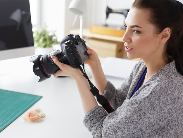 Designer di giovane donna in piedi vicino al posto di lavoro e fotografandolo con una fotocamera digitale