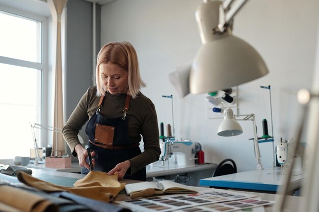 Designer femminile professionista di abiti che tagliano pezzi di pelle al tavolo