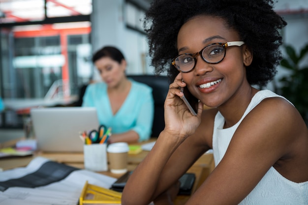 Designer grafico femminile in bicchieri sorridendo mentre parla al telefono