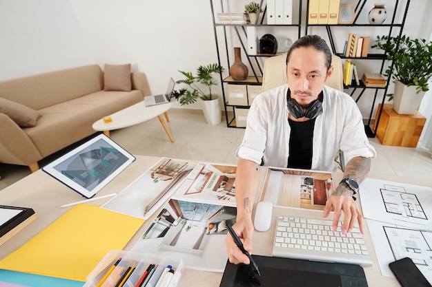 Designer professionista che lavora all'interior design di una grande casa per il cliente, è seduto a tavola con planimetrie e foto