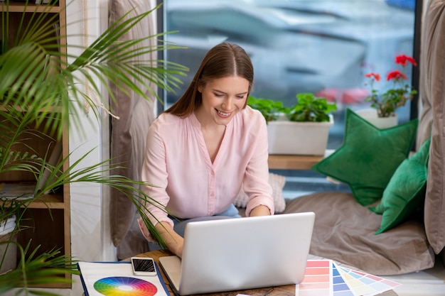 designer ragazza allegra nel suo ufficio sul posto di lavoro, lavorando su un computer portatile.