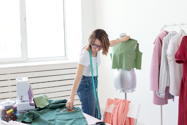 Designer sarta giovane ragazza carina con occhiali e un metro a nastro fa un nuovo prodotto con l'aiuto di un panno verde e un manichino da sarto