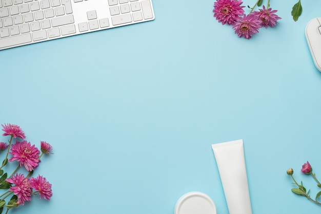 Desktop blu con tastiera e mouse rosa fiori di gerbera, blocco note e cosmetici