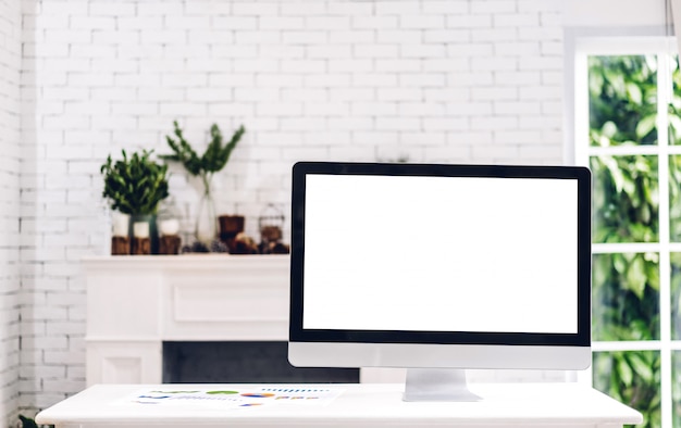 Desktop computer creativo con gli schermi in bianco bianchi sulla tavola nel sottotetto bianco minimo moderno del lavoro