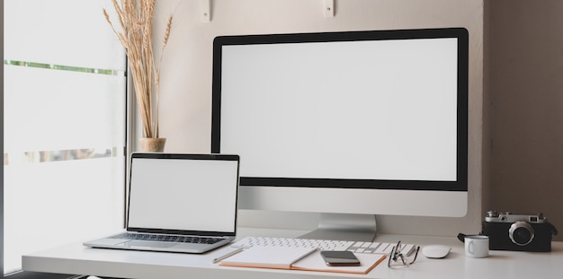 Desktop computer e computer portatile dello schermo in bianco nell'area di lavoro moderna