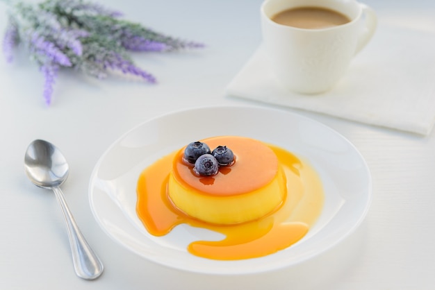 Dessert alla panna del caramello con i mirtilli in un piatto bianco e una tazza di caffè