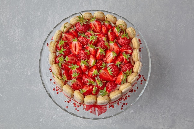Dessert con fragole biscotti savoiardi e mascarpone legati con un nastro rosso su un tavolo di cemento leggero Vista dall'alto con spazio per la copia Posa piatta