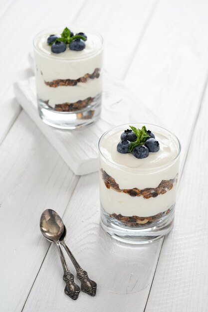 Dessert con ricotta mirtilli freschi e muesli in un bicchiere su fondo di legno bianco