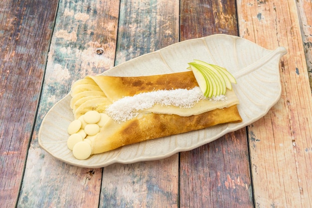 Dessert di crêpe francese ripieno di banana e mela con cioccolato bianco e cocco grattugiato