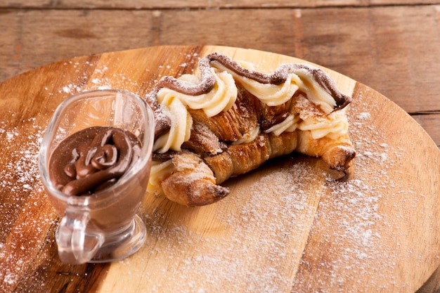 Dessert di croissant alla crema di nocciole con cioccolato bianco sul tagliere e porzione di cioccolato fuso in legno su tavola rustica in primo piano macro