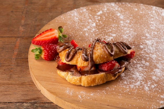 Dessert di croissant alla crema di nocciole con fragola su una tavola di legno su un tavolo rustico di fronte