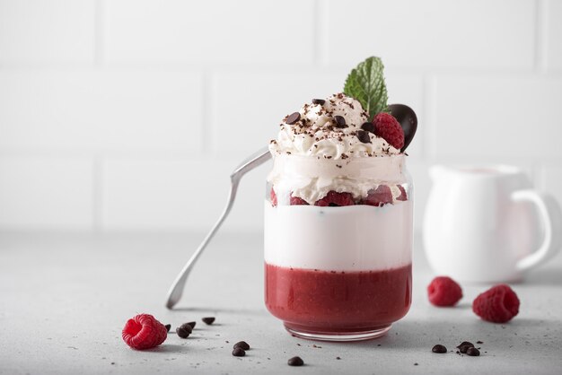 Dessert di gelatina di lamponi, panna montata e cioccolato al latte in un barattolo di vetro