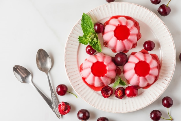 Dessert di panna cotta con ciliegie fresche, sciroppo e menta in un piatto con cucchiai. Sano cibo vegano italiano. vista dall'alto