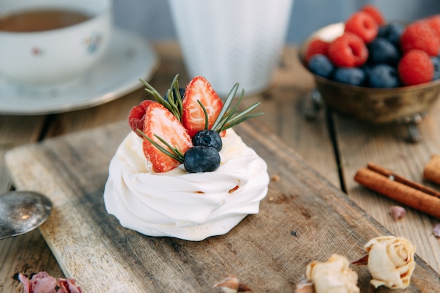 Dessert di Pavlova con fragole e mirtilli su fondo di legno Bacche dolci di meringa