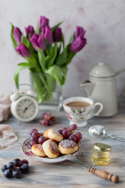 Dessert di ricotta, cheesecakes sul tavolo con un mazzo di tulipani, orologi e frutta su un tavolo di legno vicino alla finestra.