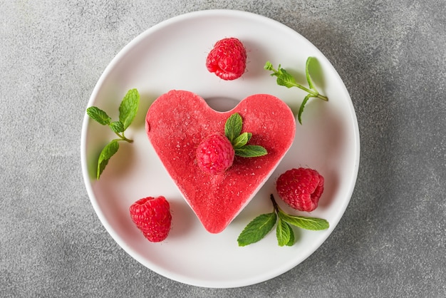 Dessert di San Valentino. cuore rosso vegan crudo a forma di cuore con lamponi e menta in un piatto. cibo delizioso e sano