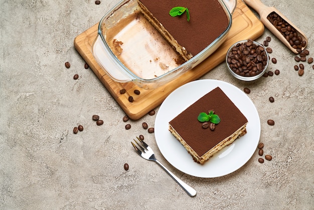 Dessert di tiramisù italiano tradizionale in teglia di vetro e porzione sul tavolo di cemento grigio