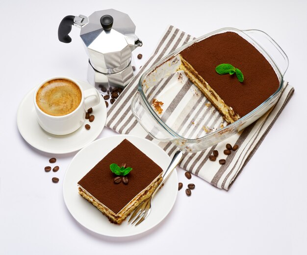 Dessert di tiramisù italiano tradizionale nella porzione di teglia di vetro sul piatto e tazza di caffè isolato su bianco