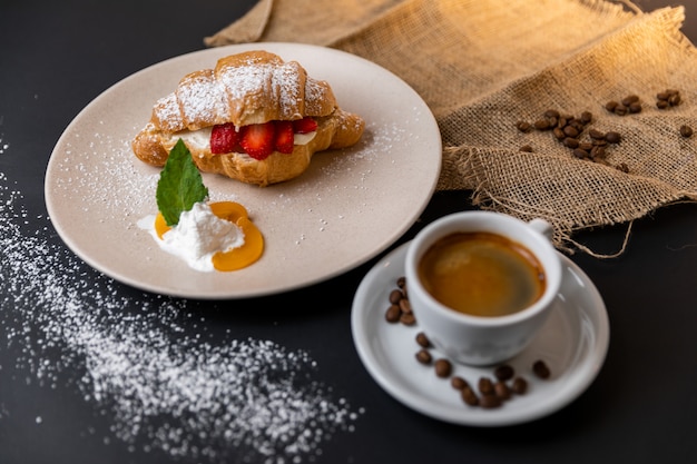 Dessert di un croissant con la fragola vicino ad una tazza di caffè