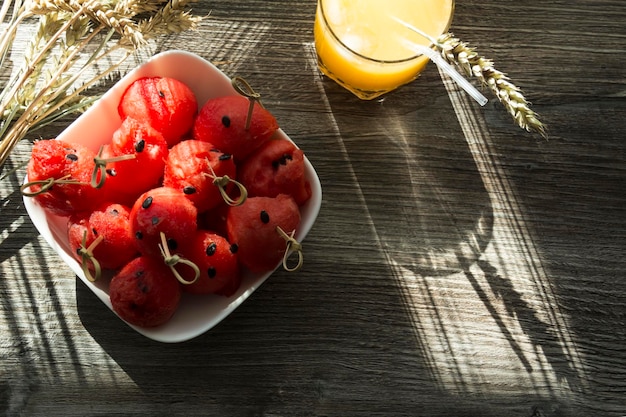 Dessert dolce dell'anguria del succo d'arancia appena spremuto e spighette di grano maturo su un tavolo di legno alla luce del sole