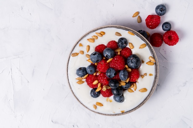 Dessert fresco saporito di scossa del yogurt di lamponi del mirtillo in ciotola ceramica che sta sulla tavola bianca