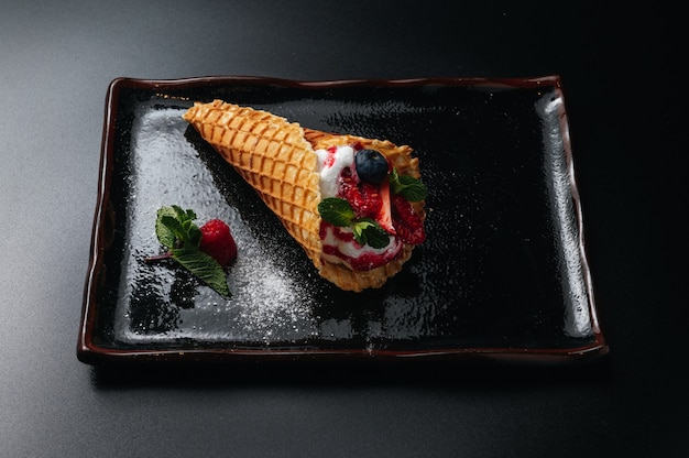 dessert gelato in cono di zucchero condita con frutti di bosco e servito su un piatto nero