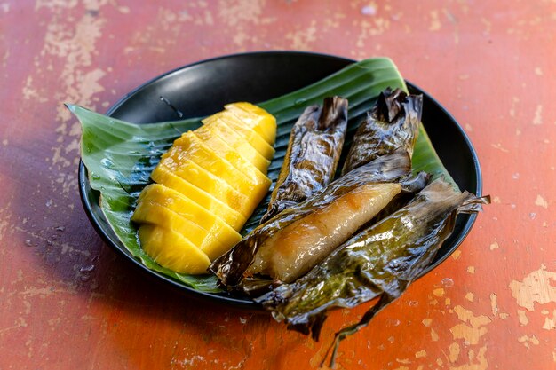 Dessert in stile tailandese, mango giallo con riso appiccicoso alla banana in foglie di palma. Il mango giallo e il riso appiccicoso sono un dolce tradizionale popolare della Thailandia. Avvicinamento