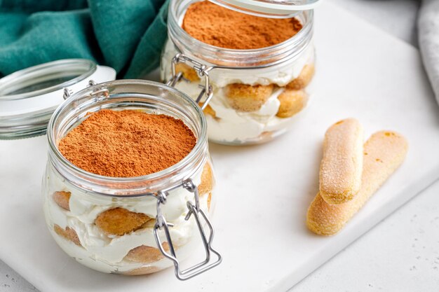 Dessert tiramisù in vasetti con coperchio su tavola di marmo e tovagliolo verde sfondo grigio Torta tiramisù