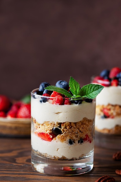 Dessert vegano in un bicchiere con frutti di bosco menta panna montata e biscotto su sfondo marrone