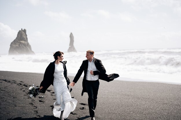 Destinazione islanda matrimonio la coppia di sposi corre lungo la spiaggia di sabbia nera di vik vicino a