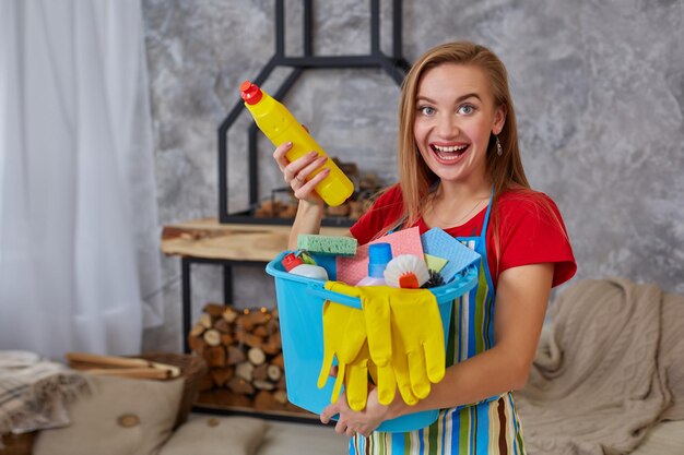 Detergente ravvicinato per la pulizia delle mani emotive della donna o della casalinga con molti oggetti domestici in un secchio blu nel soggiorno. Compiti a casa.