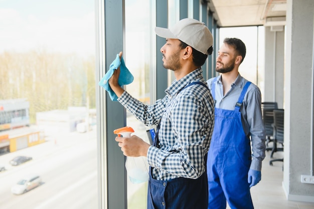 Detergenti professionali multietnici in uniforme che lavano grandi finestre in ufficio