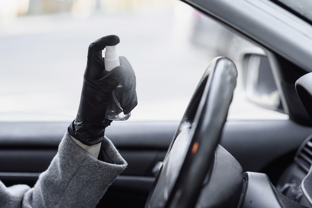 Detergere l'interno dell'auto e spruzzare con liquido disinfettante. Mani in guanti protettivi in gomma per disinfettare il veicolo all'interno per proteggere dalle malattie virali