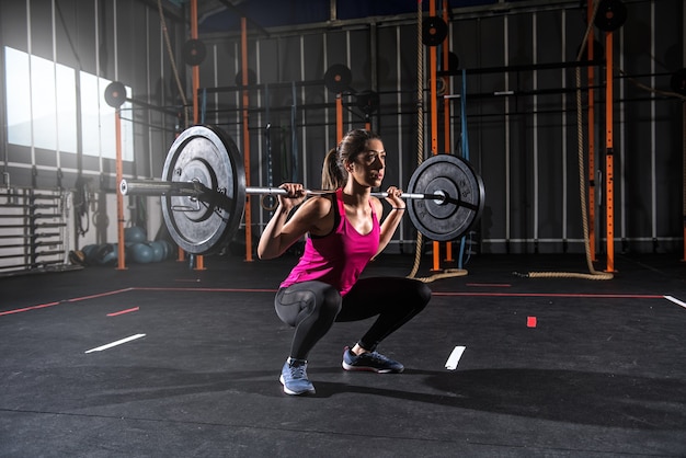 Determinata ragazza atletica lavora in palestra con un bilanciere