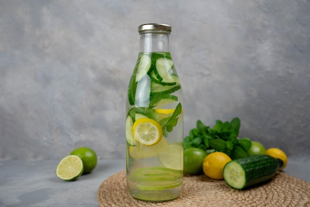 Detox Sassy acqua con limone, cetriolo, menta. Una bottiglia di bevanda pulita, fresca e fresca si trova su uno sfondo di cemento grigio con ingredienti a bordo. Rafforzamento dell'immunità, dieta. Natura morta da vicino.